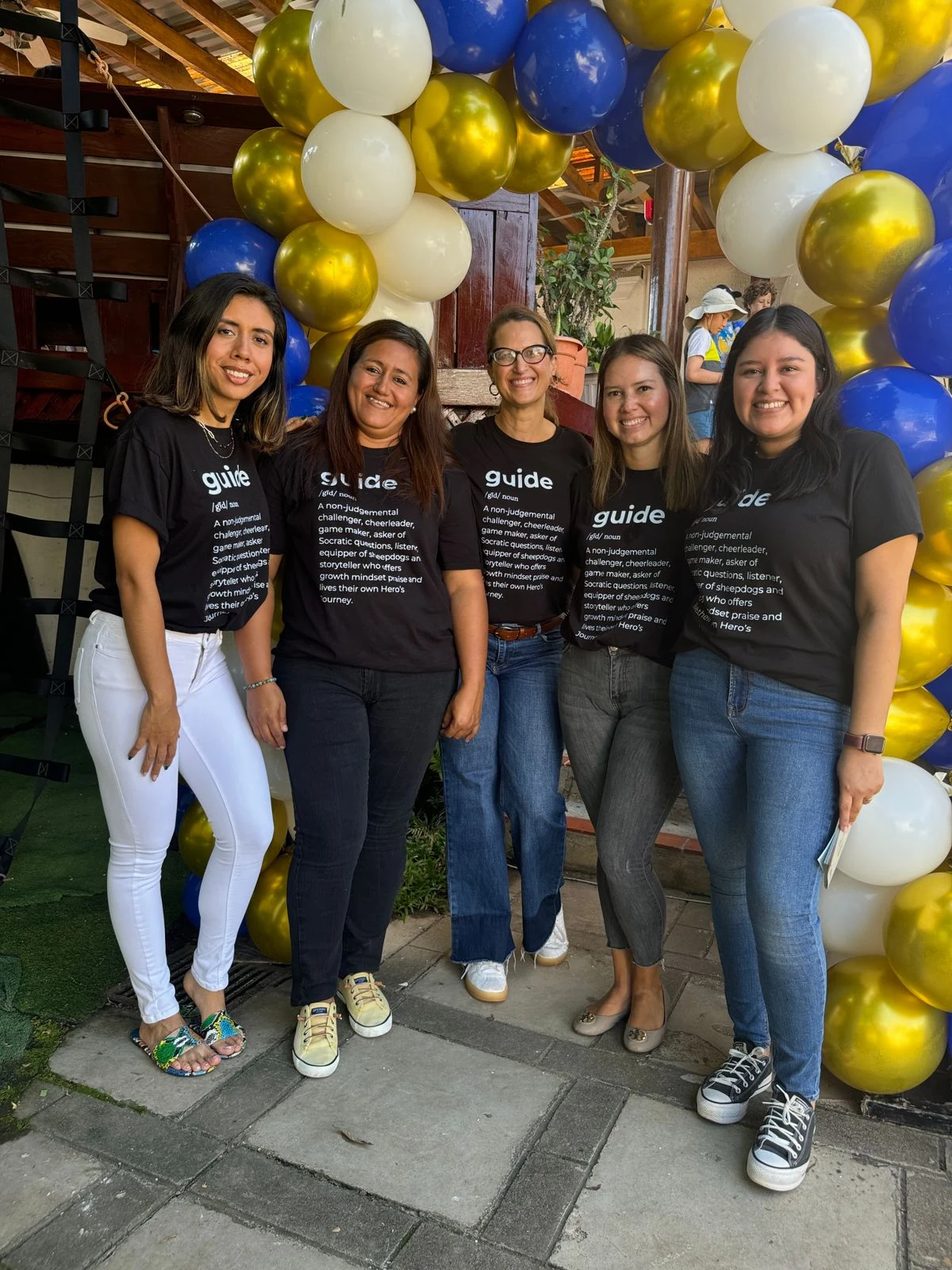Five Acton Academy guides together beneath blue, white and gold balloons