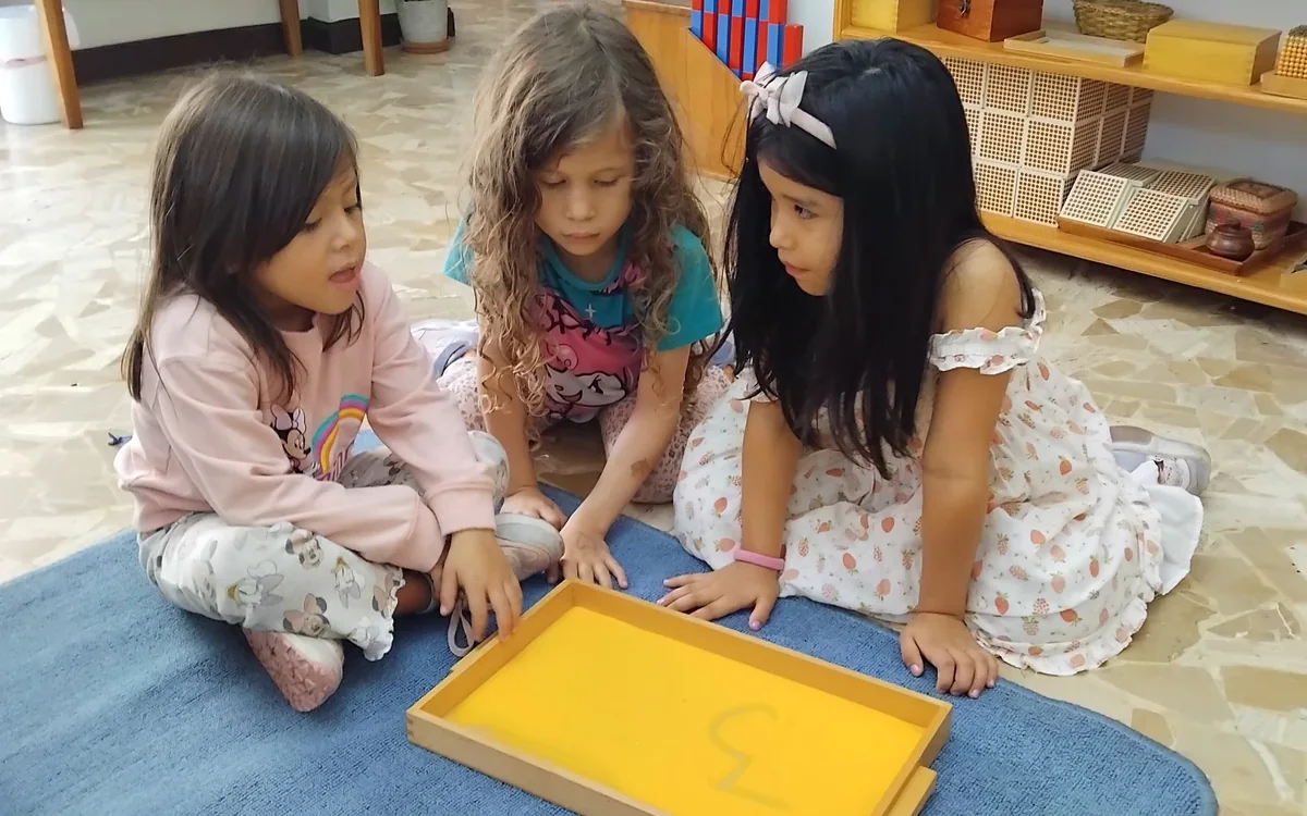 Three preschool children working together with Montessori number materials on a mat at Acton Academy El Salvador